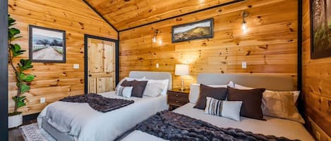 A cozy wooden cabin bedroom with two beds, a ceiling fan, and framed pictures on the walls.