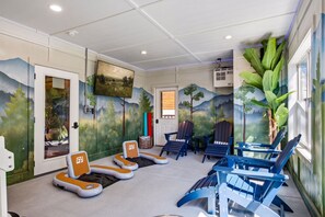 Ein Zimmer mit einem Waldgemälde, mehreren Adirondack-Stühlen und einem Massagetisch.