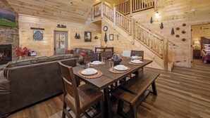Ein Holzinnenraum mit einem für vier Personen gedecktem Esstisch, einer Treppe und einem Wohnbereich mit Sofa und Kamin.