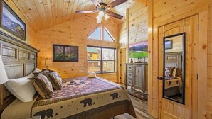 Ein Schlafzimmer in einer Holzhütte mit einem Bett, einem Deckenventilator, einer Kommode und einer Tür mit Spiegel.