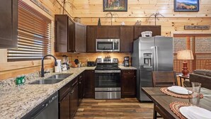 Eine Küche mit Holzausstattung, Edelstahlgeräten und Granit Arbeitsplatten, sowie ein Essbereich mit Tisch für zwei Personen.