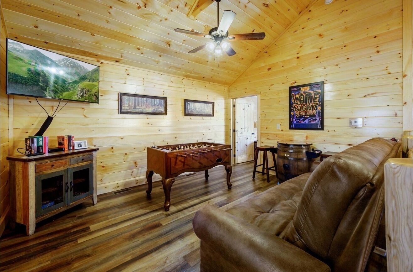 A wooden interior with a sofa, a foosball table, a television, and a ceiling fan.