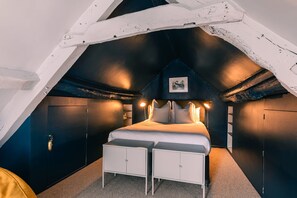 A bedroom with a sloped ceiling, a bed with white bedding, two bedside tables, and a small picture on the wall. - Lavish Farmhouse With Lake Gardens Pool Table (Radstock)