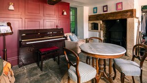 A room with a piano, a round table, and a fireplace. - Lavish Farmhouse With Lake Gardens Pool Table (Radstock)