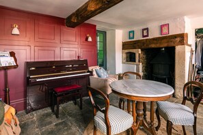 A room with a piano, a round table, and a fireplace. - Lavish Farmhouse With Lake Gardens Pool Table (Radstock)