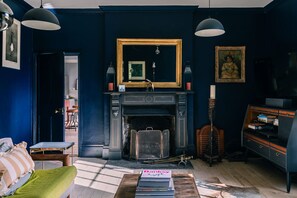 A room with a fireplace, a mirror, a green sofa, and a bookshelf. - Lavish Farmhouse With Lake Gardens Pool Table (Radstock)