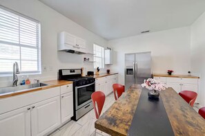 A modern kitchen with white cabinets, a stainless steel refrigerator, and a wooden dining table with red chairs. - Comfortable & Contemporary 3BR/2BA House - 5 Minutes to Downtown Austin (Austin)
