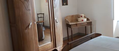 A bedroom with a wooden wardrobe, a bed, a small table with a cup, and a chair.