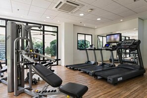 A gym with exercise equipment, treadmills, and a large window. - The Universe Executive Flat (São Paulo)