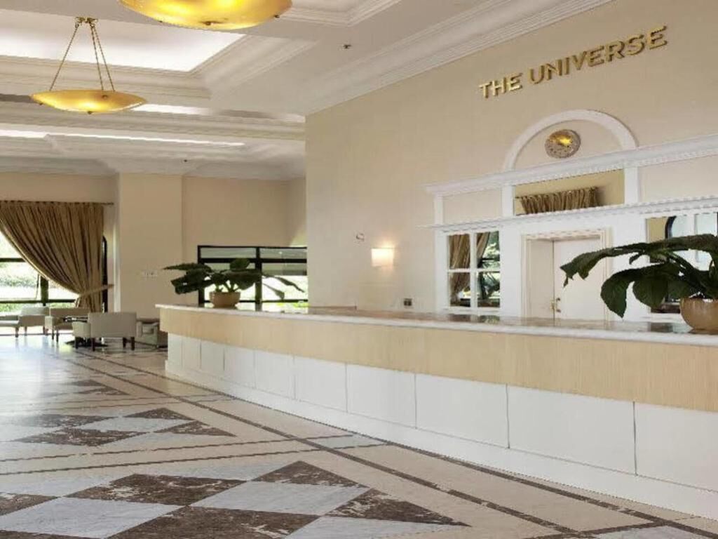 Un hall d’hôtel avec un comptoir d’accueil, une grande plante en pot et une enseigne murale sur laquelle on peut lire : « L’UNIVERS ».