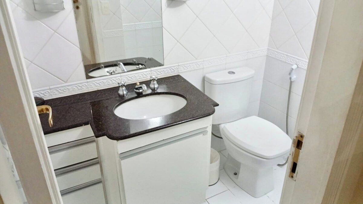 Un baño con inodoro blanco, lavamanos con encimera negra y espejo sobre el lavamanos.