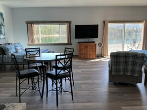 A living room with a round dining table, chairs, a sofa, a TV, and a sliding glass door leading to an outdoor area. - HIDE-A-WAY SUITE RETREAT … Just Steps Away From shoreline on Bitterroot Lake (Marion)