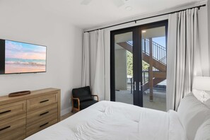 A bedroom with a bed, a wooden dresser, a chair, a TV, and a view of the outside.