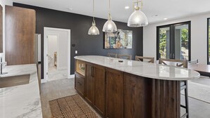 Eine moderne Küche mit Marmorarbeitsplatte, Holzschränken und Pendelleuchten.