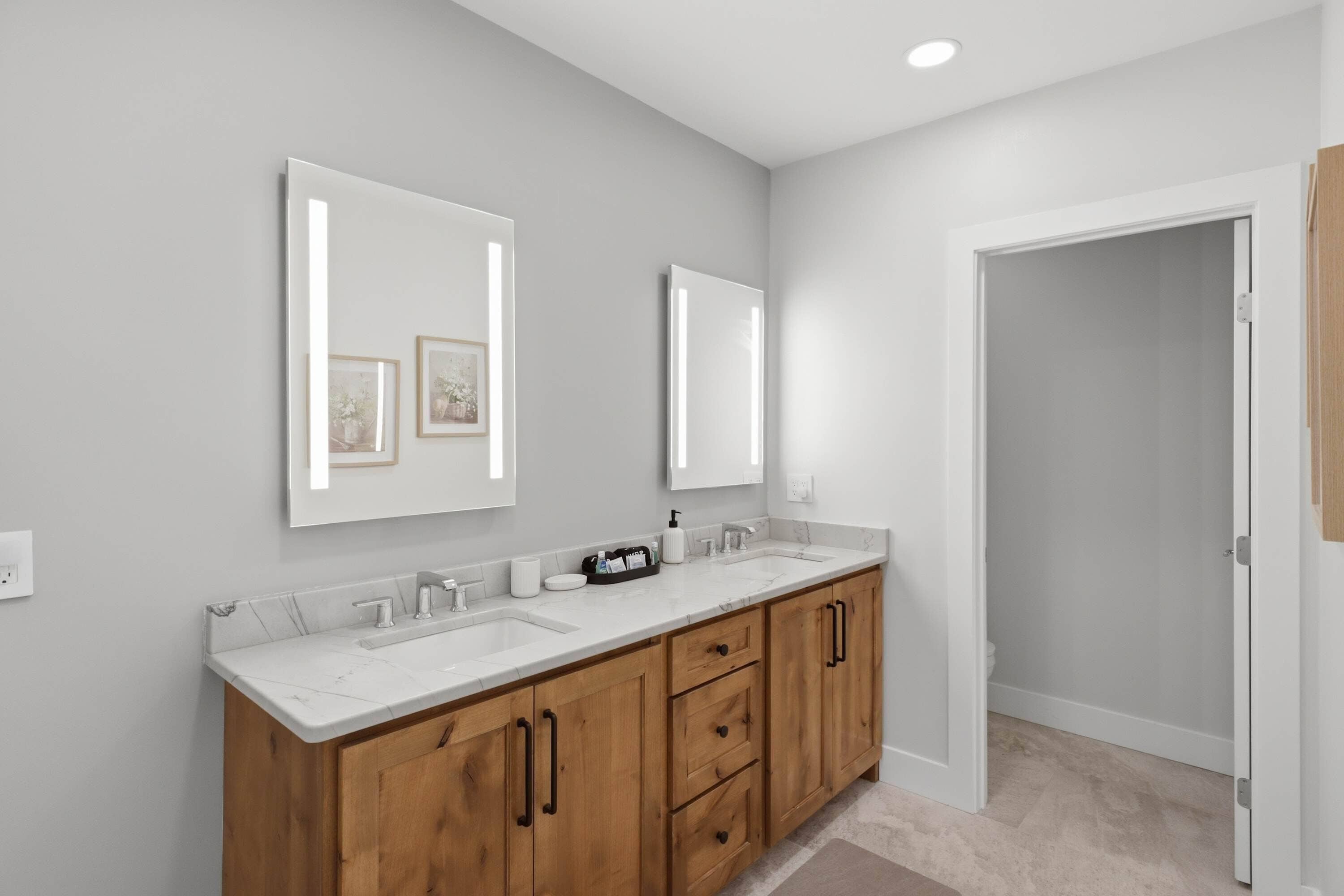 A modern bathroom with a double vanity, marble countertops, wooden cabinets, and wall-mounted mirrors.