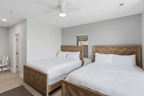 A bedroom with two single beds, a ceiling fan, a window with blinds, and a door.