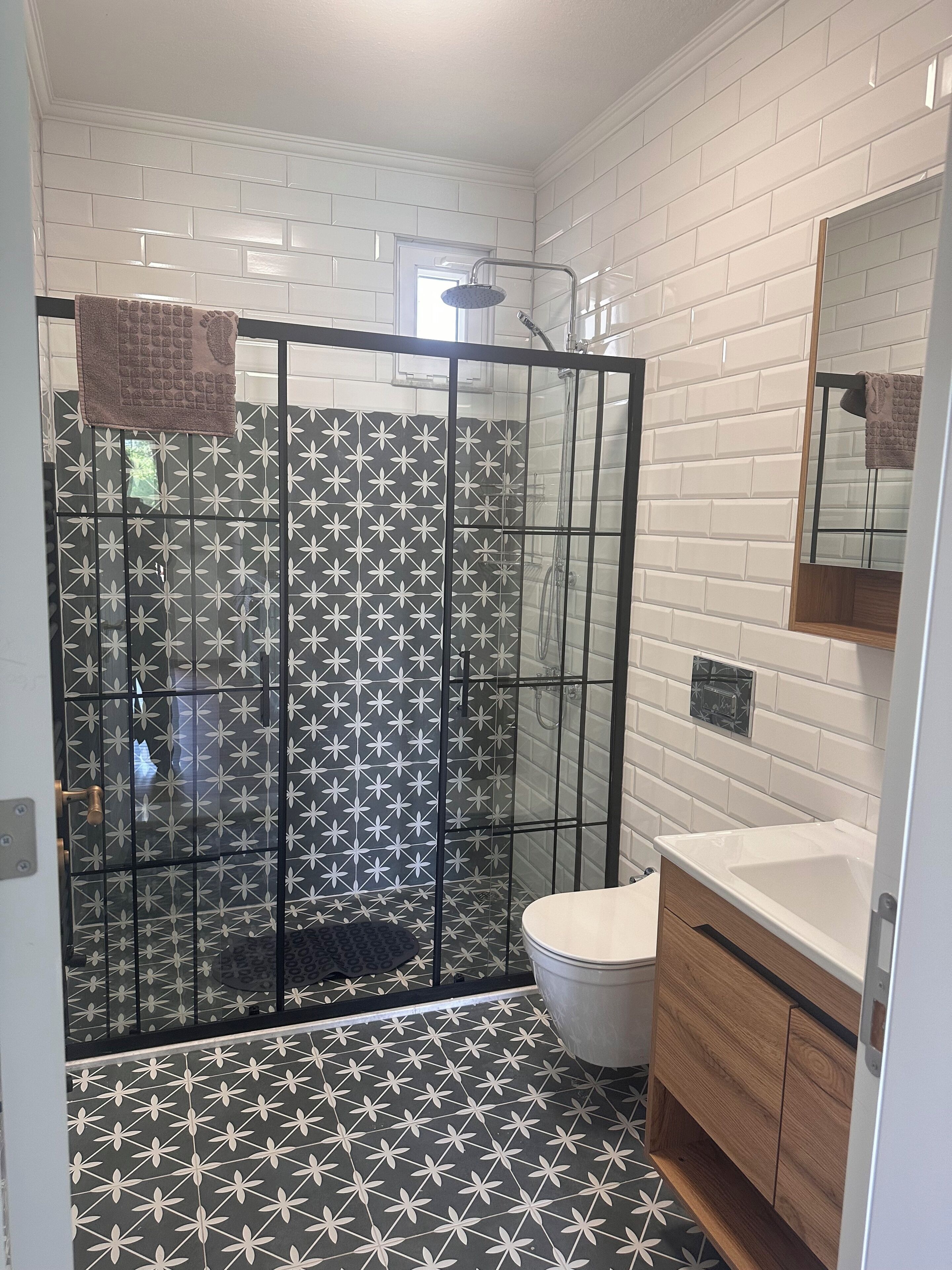 A bathroom with a shower enclosure, a toilet, a sink, and a mirror.