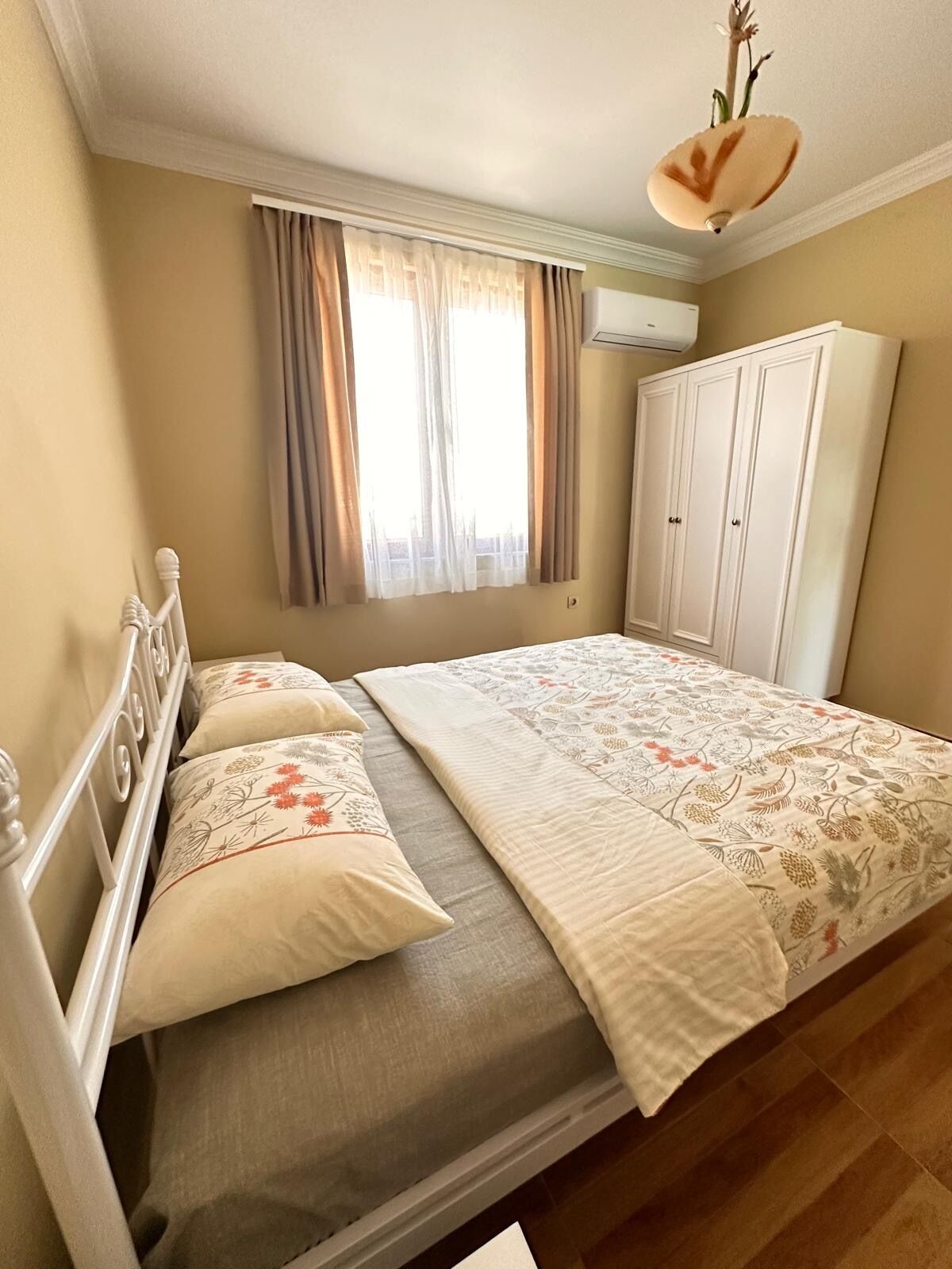 A bedroom with a bed, a wardrobe, a window with curtains, and an air conditioning unit.