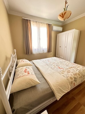 A bedroom with a bed, a wardrobe, a window with curtains, and an air conditioning unit.