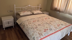 Una cama con edredón estampado, una mesita de noche blanca, un cajón y un enchufe de pared.