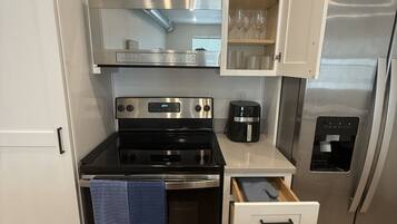 Uma cozinha compacta com armários brancos, fogão de aço inoxidável, forno embutido, cafeteira e geladeira.
