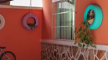 Um quarto com parede de pedra, janela com grades de metal, uma bicicleta e um pneu pendurado como vaso de plantas.