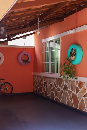 A room with a stone wall, a window with metal bars, a bicycle, and a tire hanging as a planter. - A very cozy house near the center of Belo Horizonte with a garage. (Belo Horizonte)