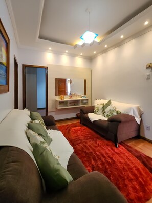 A modern living room with a sofa, a red rug, a mirror, and a ceiling light fixture. - A very cozy house near the center of Belo Horizonte with a garage. (Belo Horizonte)