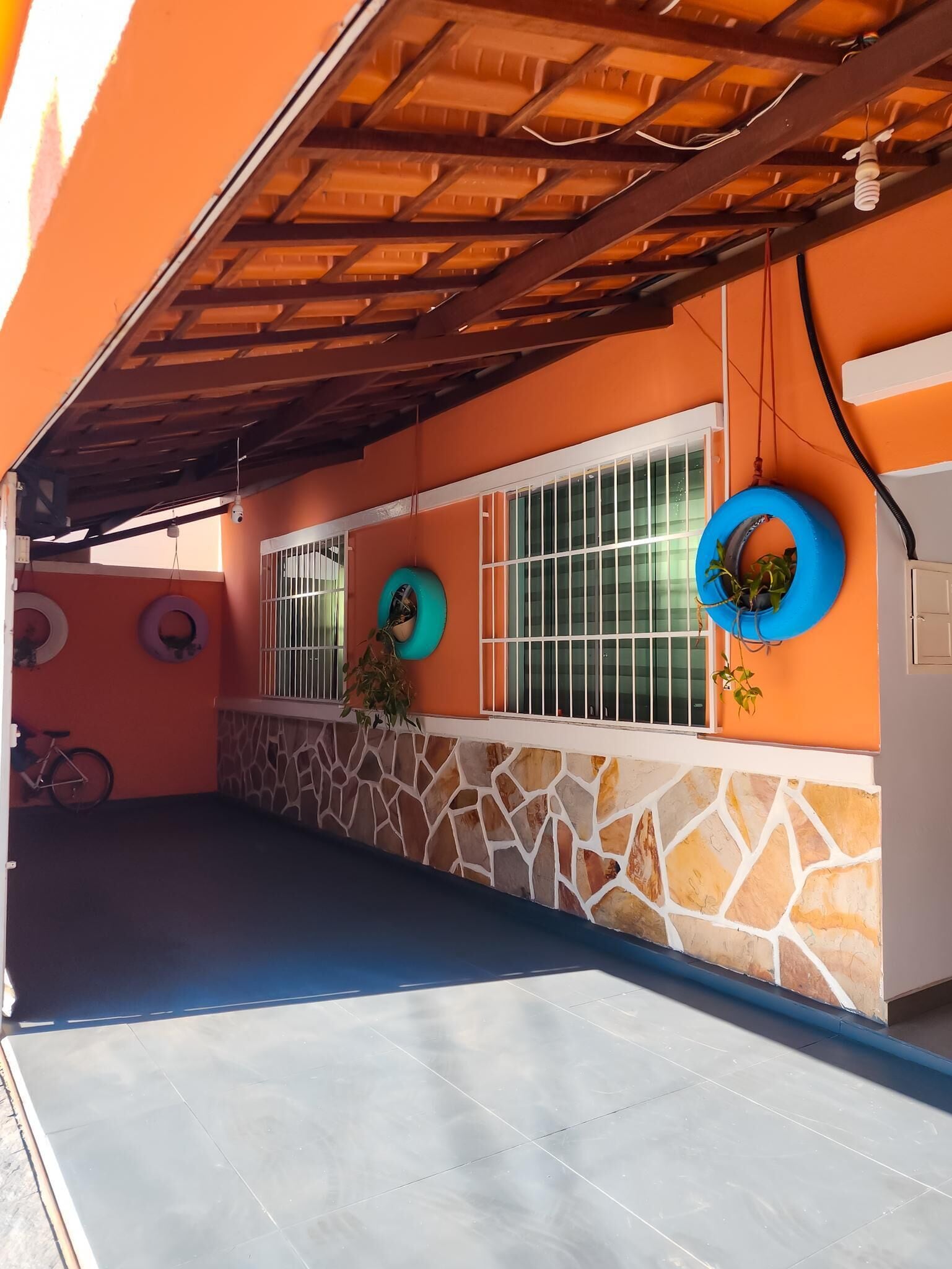Uma área externa coberta com parede de pedra, uma bicicleta e um pneu pendurado na parede.