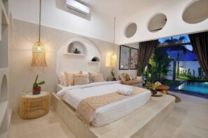 A modern bedroom with a large bed, a small seating area, a pool, and a view of the outdoors. - 3 Bedroom Luxury Villa Blue Mango Umalas Canggu (Badung Regency)