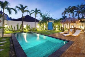 A swimming pool with a wooden deck and lounge chairs, surrounded by palm trees and a blue door. - 3 Bedroom Luxury Villa Blue Mango Umalas Canggu (Badung Regency)