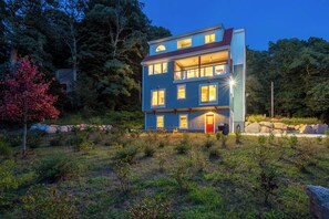 Un edifici de diversos pisos amb un balcó al segon pis, envoltat d'arbres i una paret de pedra.