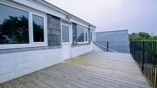 En boligbygning med en træterrasse, hvide facader og et metalhegn.
