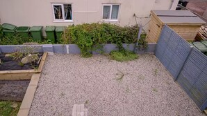 En have bag et hus med et grusområde, et forhøjet træbed og et træhegn.