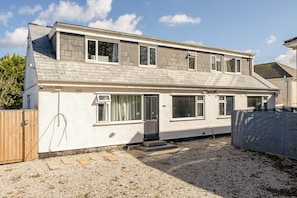 A two-story residential building with a sloped roof, multiple windows, and a gravel driveway. - 1 Bedroom Apartments Sleeps 3 - Balcony - Pets Ok (St Ives)