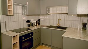 Et kompakt køkken med lysegrå skabe, en sort ovn, en vask med guldfarvet vandhane og en brødrister på bordpladen.