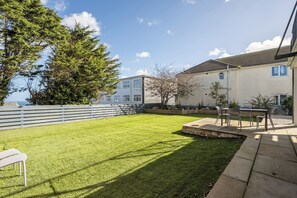 Ein Wohnhaus mit gepflegtem Rasen, einer Terrasse mit Gartenmöbeln und Meerblick.