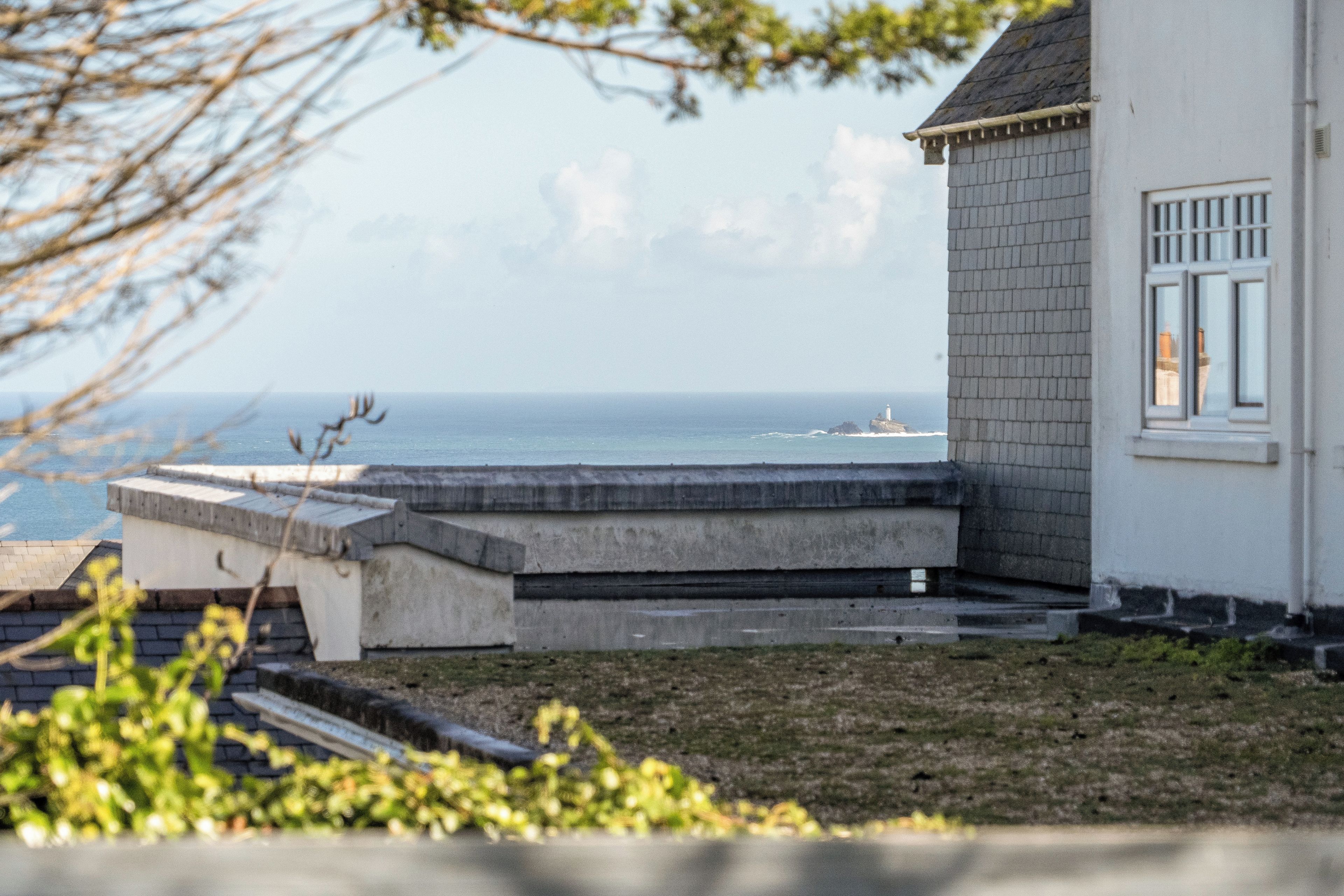 A coastal house with a view of the sea, a concrete staircase, and a small garden area.