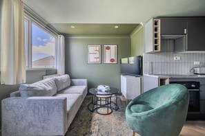 A compact living space with a sofa, a green armchair, a small table with books, a television, and a kitchen area. - 1 Bedroom Apartments Sleeps 3 - Balcony - Pets Ok (St Ives)