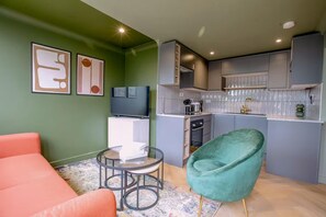 A compact living space with a kitchenette, a television, a sofa, and a green chair. - 1 Bedroom Apartments Sleeps 3 - Balcony - Pets Ok (St Ives)