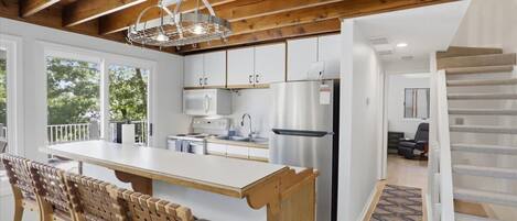 A modern kitchen with wooden beams, a central island, and a view of the outdoors.