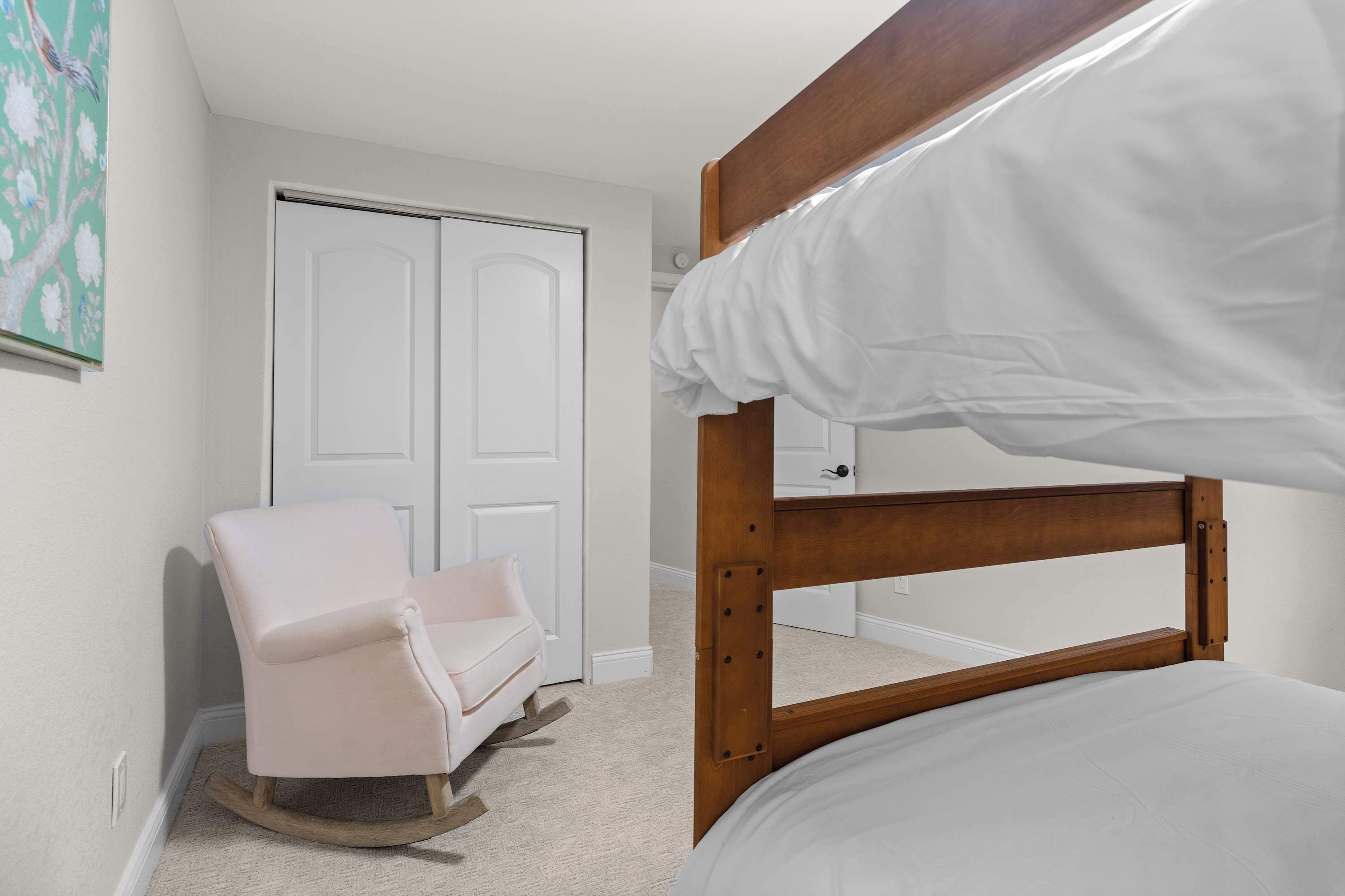 A bedroom with a bunk bed, a rocking chair, a closet, and a painting on the wall.