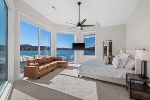 Un dormitorio con una cama grande, un sofá, un televisor y un balcón con vistas al agua.