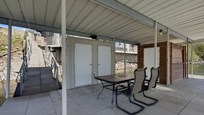 Eine überdachte Terrasse mit Tisch und Stühlen, eine Treppe zu einer Außenterrasse und Blick auf ein Gewässer.