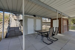 A covered patio with a table and chairs, a staircase leading to a deck, and a view of a body of water. - Sunrise Shores Estate - 4bd-4ba Luxury Lakefront (Camdenton)