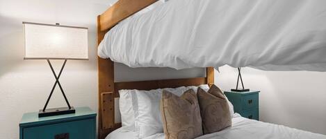 A bedroom with a bunk bed, a bedside table with a lamp, and a nightstand with drawers.