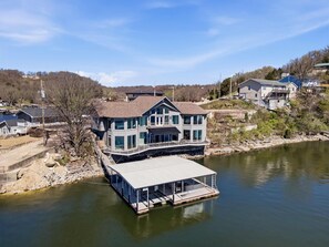A large house with a dock extending into a lake, surrounded by other houses. - Sunrise Shores Estate - 4bd-4ba Luxury Lakefront (Camdenton)