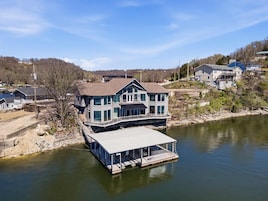 Una casa grande con un muelle que se adentra en un lago, rodeada de otras casas.