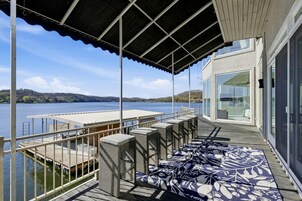 Un espacio al aire libre techado con vista a un lago, una terraza de madera y un ventanal de vidrio que da a un edificio.