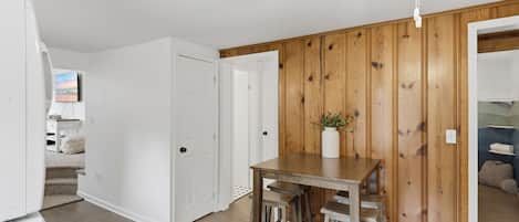 A room with a wooden wall, a white door, a table with chairs, and a ceiling fan.